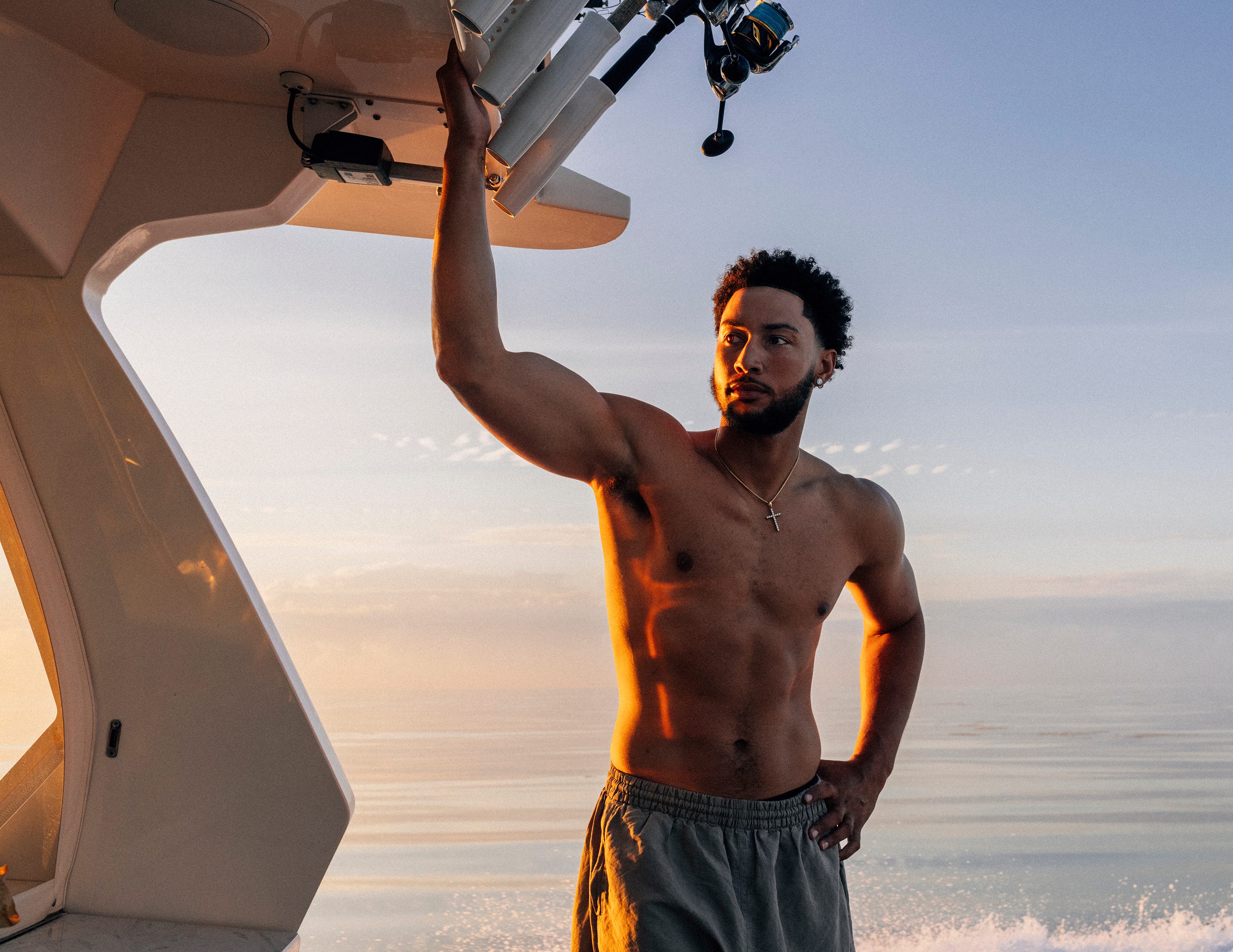 Man standing shirtless on a boat at sunrise.