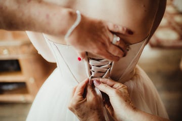 bride getting dressed for wedding ceremony having dress laced up