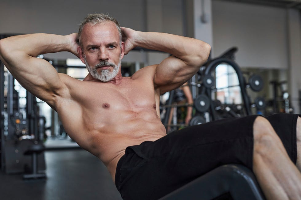 shirtless mature man doing curl up exercise in gym