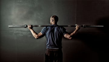 man in gym gym with weight bar on shoulders
