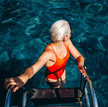 Woman with white hair wearing a red swimsuit steps into a sea, enjoying a refreshing swim on a sunny day. woman with white hair wearing a red swimsuit steps into a sea, enjoying a refreshing swim on a sunny day.