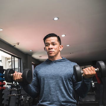 A fit asian man in a sweatshirt does seated dumbbell curls. Working out and training biceps. Open air gym setting. a fit asian man in a sweatshirt does seated dumbbell curls working out and training biceps open air gym setting
