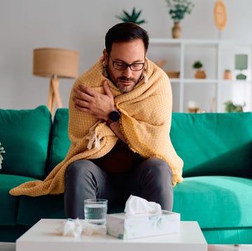 man feeling sick and unwell, wrapped in a warm blanket on the sofa, experiencing a cold or flu with tissues and a glass of water nearby, needing rest and recovery man feeling sick and unwell, wrapped in a warm blanket on the sofa, experiencing a cold or flu with tissues and a glass of water nearby, needing rest and recovery