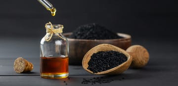 Glass bottle of black cumin seed essential oil , Nigella Sativa in scoop on black wooden background, oil dripping glass bottle of black cumin seed essential oil , nigella sativa in scoop on black wooden background, oil dripping