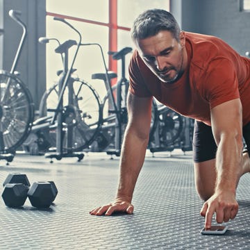 Shot of a mature man selecting music from his cellphone before doing mountain climbers during his workout shot of a mature man selecting music from his cellphone before doing mountain climbers during his workout